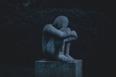 A solitary statue of a curled-up human figure, sitting on a pedestal in the dark, evoking feelings of loneliness and introspection