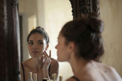 Woman looking in a mirror with concern about facial blemishes, reflecting self-image anxiety