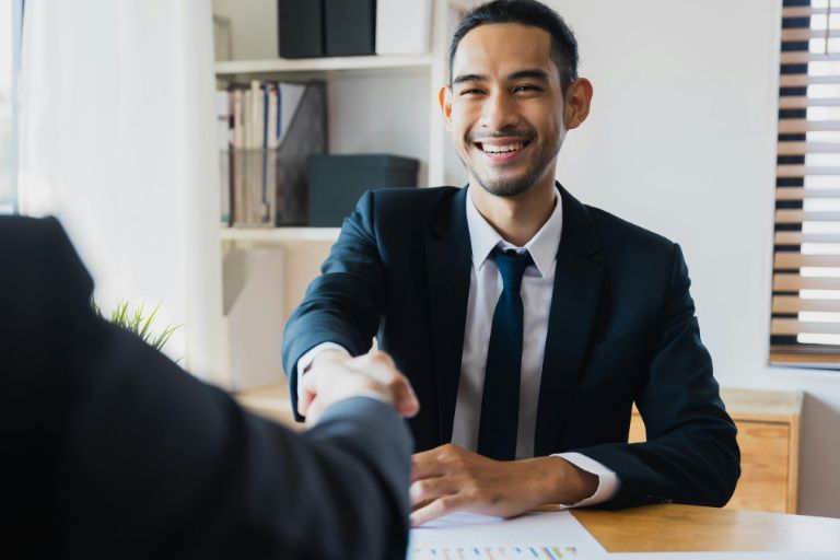 A confident man in a suit smiling and shaking hands during a meeting, symbolizing decisiveness and self-assurance