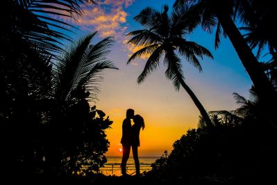 Silhouette of a couple kissing at sunset on a tropical beach, surrounded by palm trees, representing the passion and idealism often felt during the early honeymoon phase of a romantic relationship