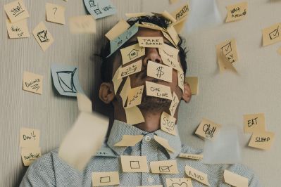 A man leaning against a wall with sticky notes all over his face and body, symbolizing work overload and mental exhaustion