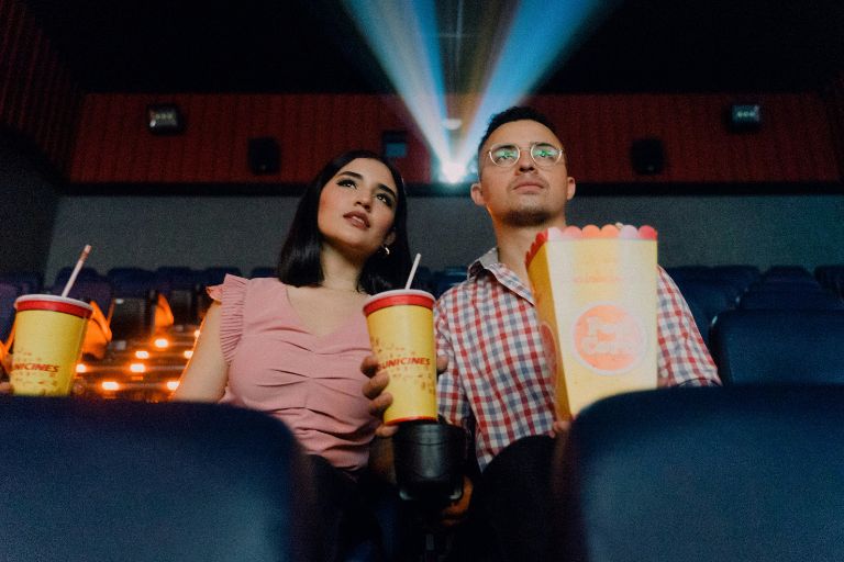 Young couple enjoying movies at cinema theater with popcorn and drinks, representing the shared cultural experience of finding wisdom and life lessons through films