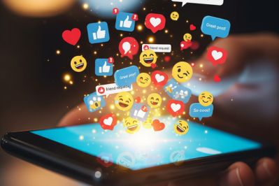 Close-up of a smartphone with social media notifications, likes, comments, and emoji reactions bursting from the screen, representing digital overwhelm and online engagement
