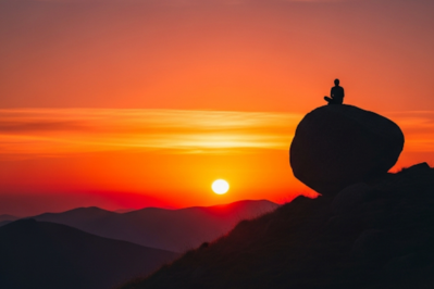 Silhouette of a person meditating on a boulder at sunset, symbolizing inner peace, passion, and alignment with purpose