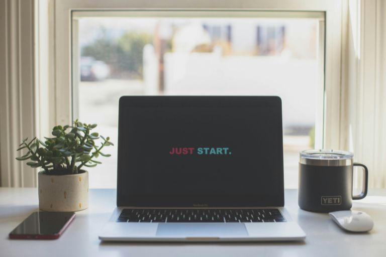 A laptop on a desk displaying the motivational phrase 'Just Start,' symbolizing imperfect action and the first step toward mastery