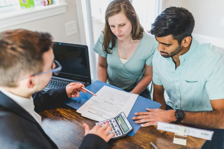 A financial advisor meeting with a couple to review financial documents and calculate expenses at a desk