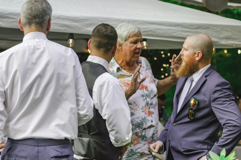 Group of well-dressed men having an animated conversation at an outdoor social event under string lights