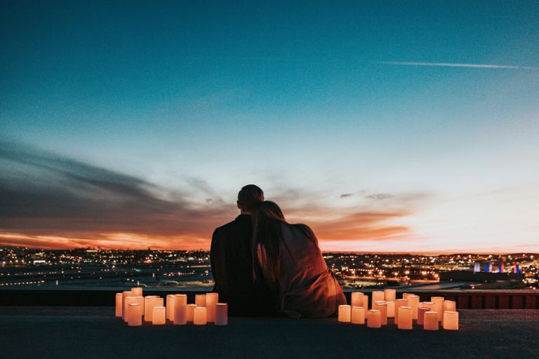 Silhouette of couple embracing at sunset with lit candles overlooking city lights showing intimate romantic connection