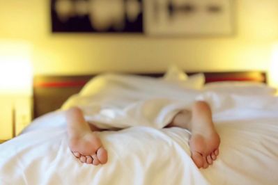Person's feet sticking out from under white bed covers while lying in bed